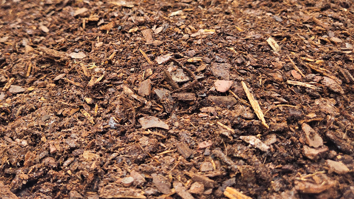 A close-up view of rich pine fines soil amendment with visible wood chips, soil, and organic fragments filling the frame.