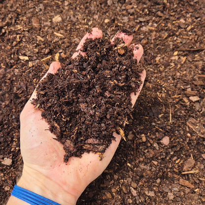 A hand holding Pine Fines soil amendment above a garden bed with fresh soil.